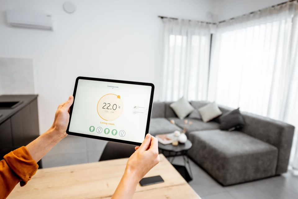 Intérieur moderne avec personne tenant une tablette affichant interface de contrôle domotique température 22°C salon