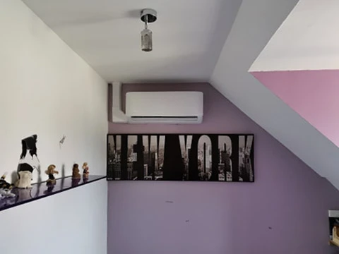 Intérieur résidentiel moderne avec climatiseur mural installé sur mur blanc entre deux fenêtres offrant vue sur jardin extérieur verdoyant