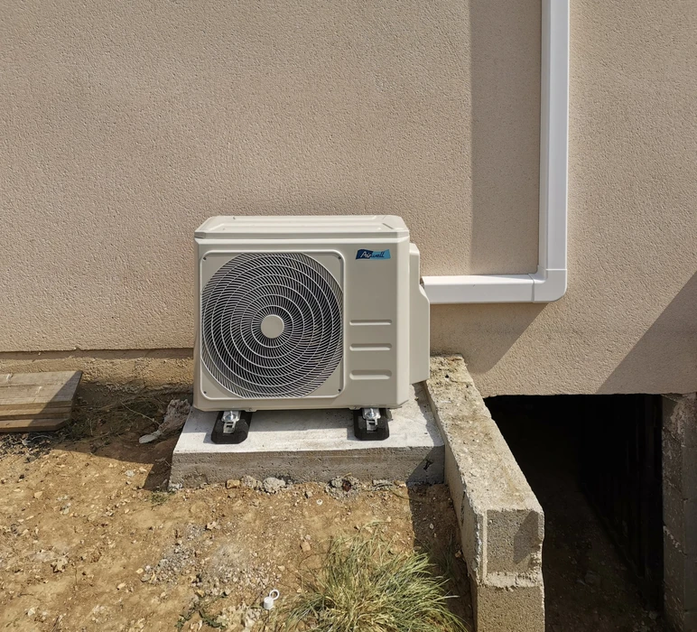 Intérieur résidentiel moderne avec climatiseur mural installé sur mur blanc entre deux fenêtres offrant vue sur jardin extérieur verdoyant