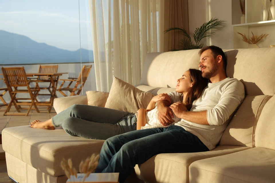 Couple assis sur canapé gris dans salon moderne, homme tenant télécommande climatiseur, femme à côté